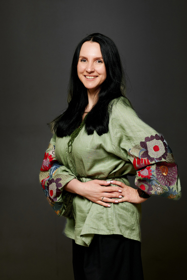 Young woman with long dark hair wearing a gray blazer, resting her head on her hand against a plain background.